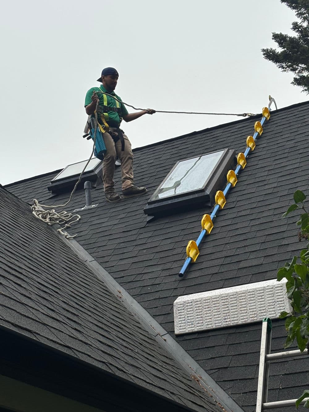 Roofer in harness on a sloped roof installing safety equipment near skylights.