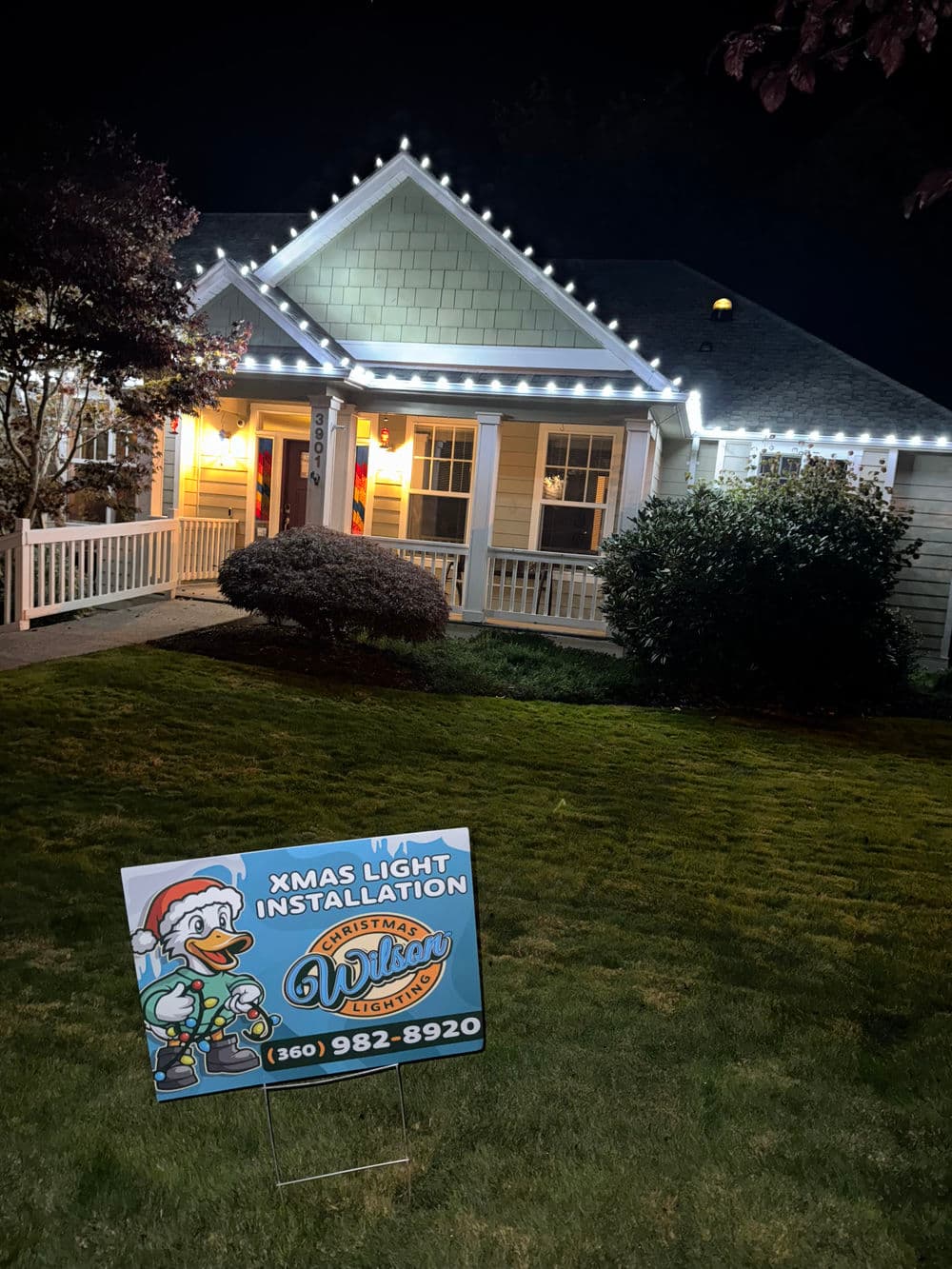 Christmas light installation sign in front of a beautifully decorated home at night.