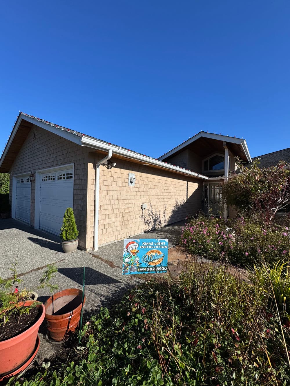 Single-story modern home with landscaping and for sale sign in front, under clear blue sky.