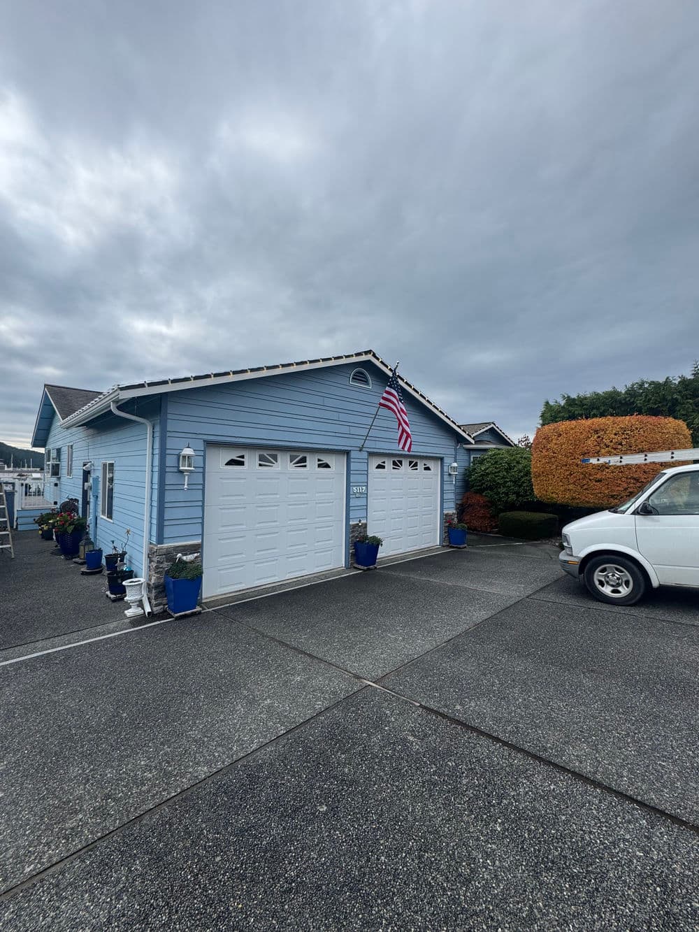 Blue house with two garage doors, American flag, and landscaped front yard on a cloudy day.