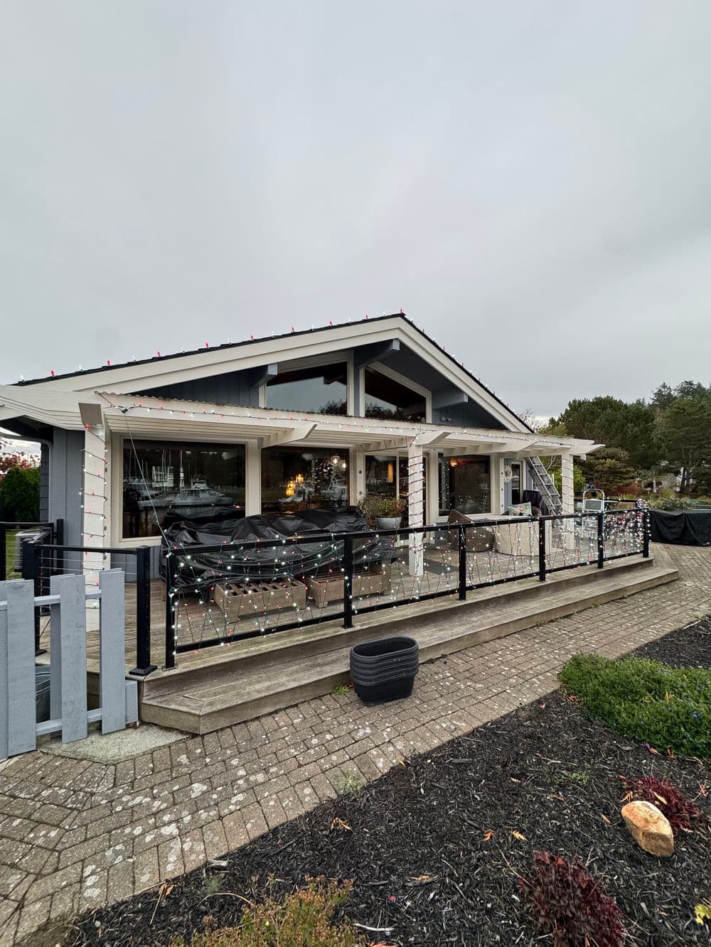 Cozy restaurant with festive lights, outdoor seating, and panoramic windows on a cloudy day.